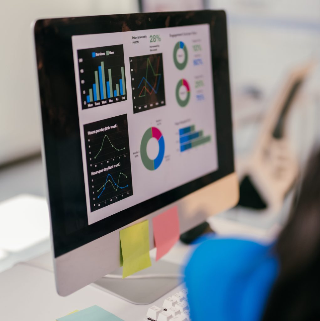 Focused businesswoman analyzes financial data on her computer, using graphs to plan for growth. Her cluttered desk shows her dedication to success