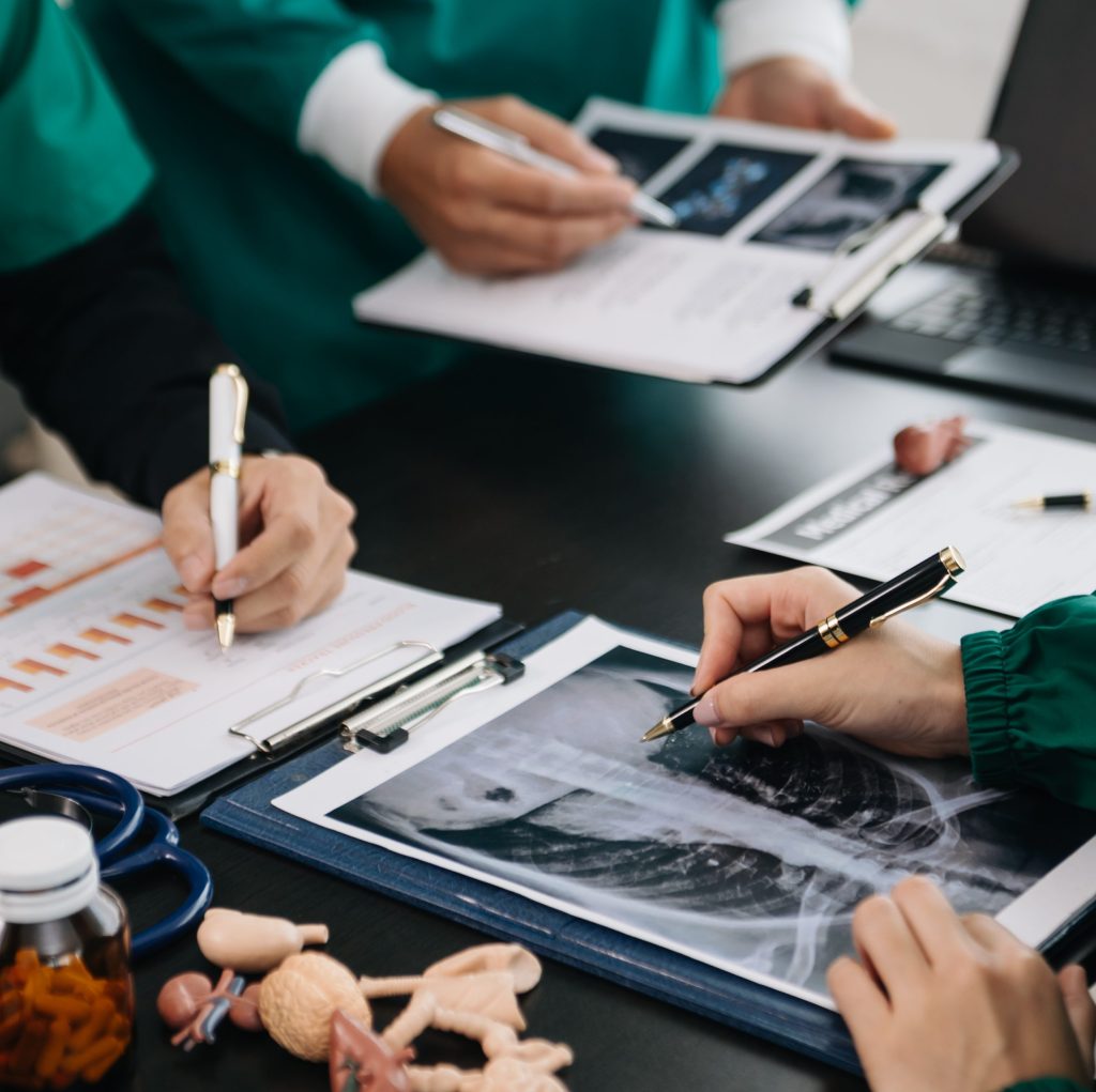 Medical team having a meeting with doctors in white lab coats and surgical scrubs seated at table discussing a patients working online using computers in the medical industry